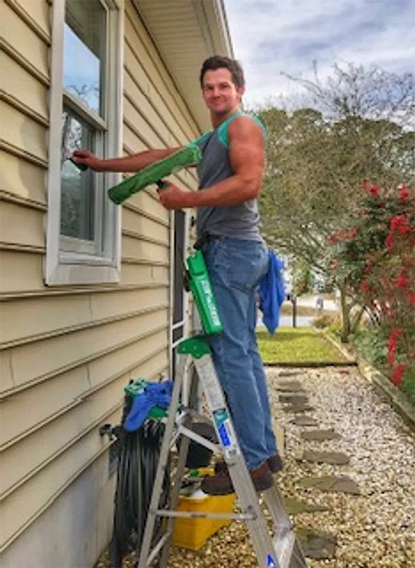 A man is standing on a ladder cleaning a window.