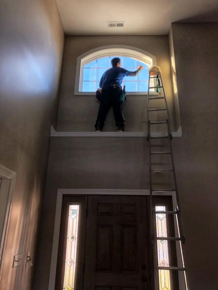 A man is standing on top of a ladder cleaning a window.