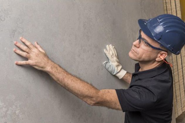 Construction worker in hard hat inspecting a gray wall with gloved hands