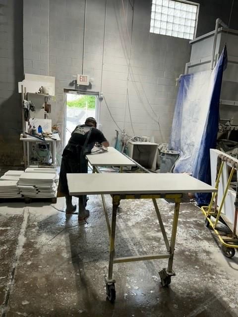 Person sanding a light-colored countertop inside a workshop