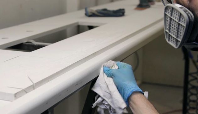 Person in blue gloves wiping a white countertop edge with a cloth