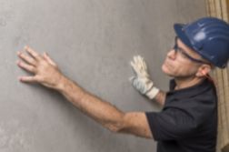 Construction worker in hard hat and gloves inspecting a concrete wall with his hands.
