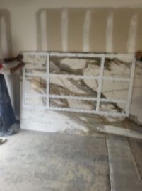 A large stone slab with a white metal frame, likely a countertop, being held by two people in a garage.