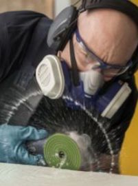 Person using a grinder, wearing safety glasses, earmuffs, and a respirator, with water spraying.