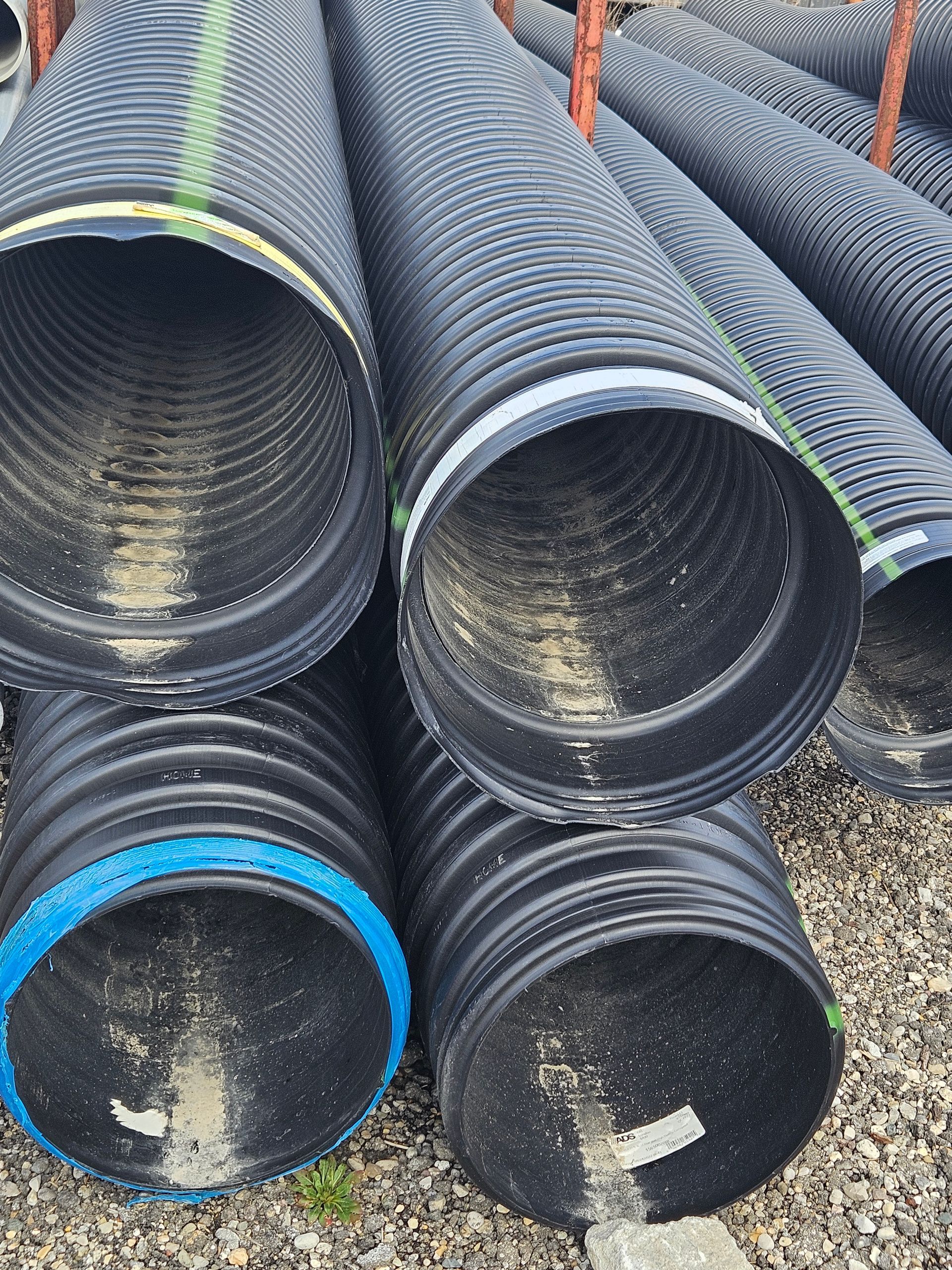 Stacked black corrugated drainage pipes with colored bands, viewed from the open ends.