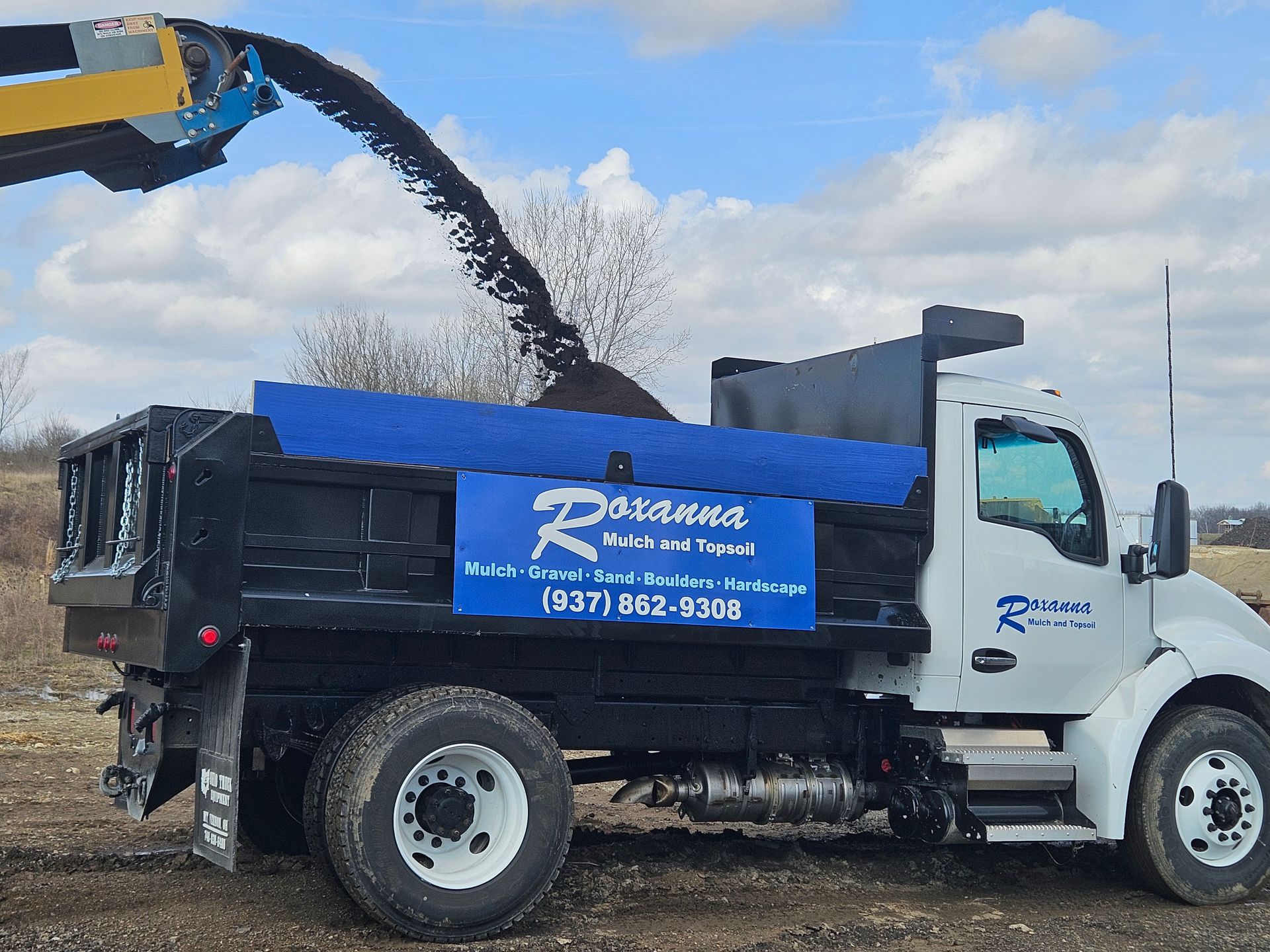 White dump truck being loaded with dark gravel from a yellow excavator under a blue sky