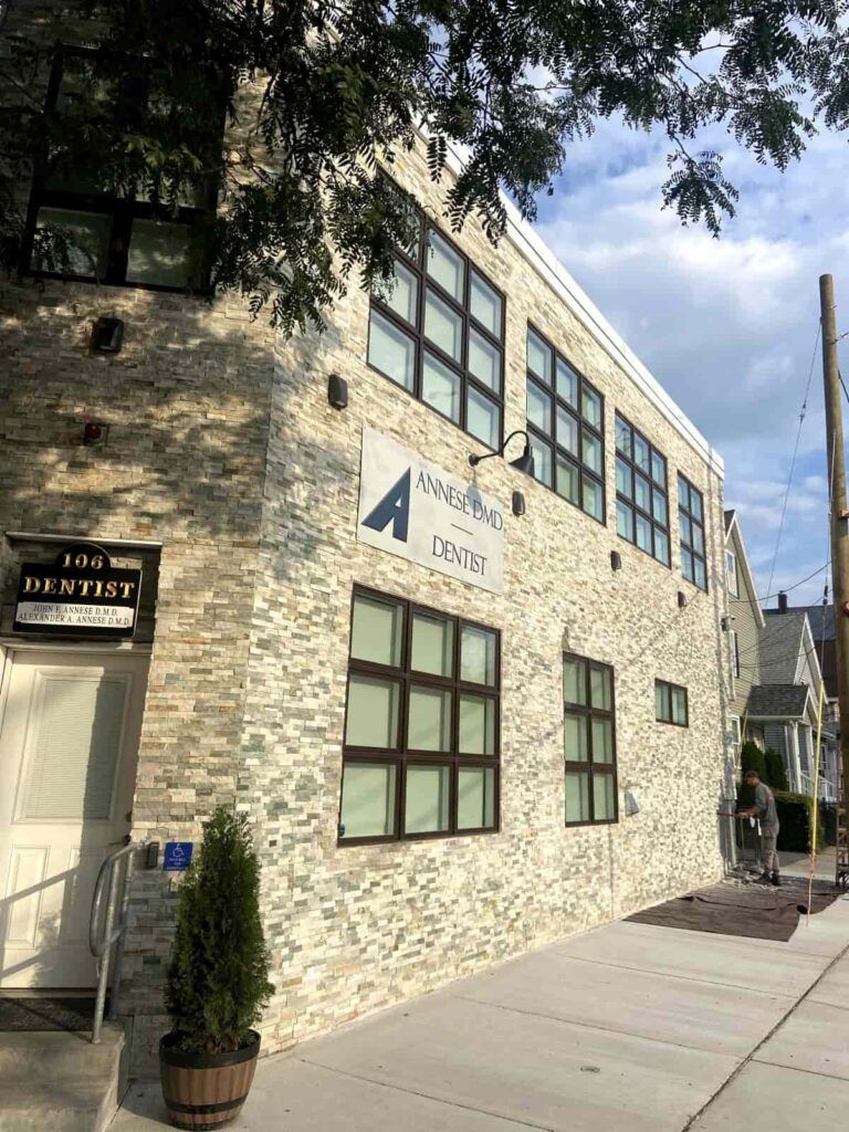 Exterior of a dental office with stone facade, dark-framed windows, and a sign that reads