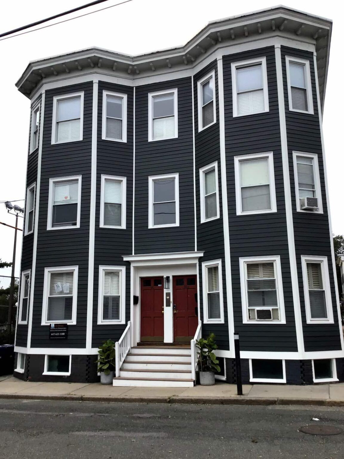Two-story dark gray building with white trim, red doors, and multiple windows.