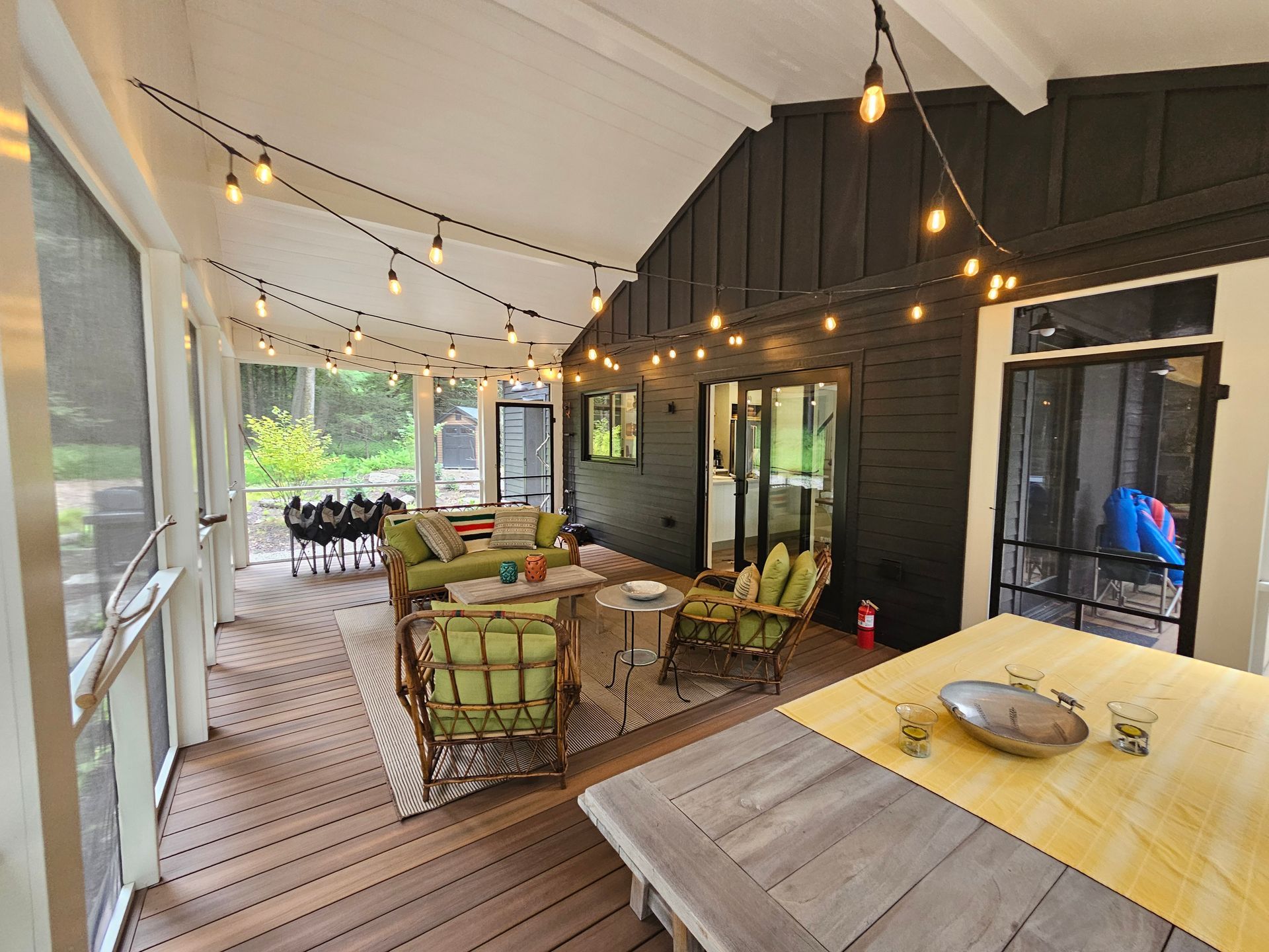 A screened-in patio featuring a wooden deck, comfortable seating, a dining area, and string lights overhead.