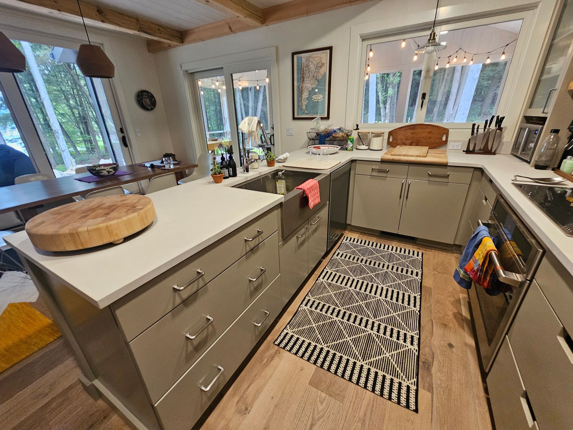 A modern kitchen with light grey cabinets, a farmhouse sink, white countertops, and a black and white patterned rug.