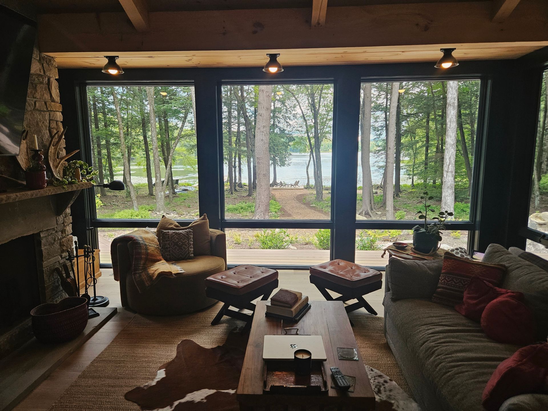A cozy living room with a fireplace, comfortable seating, and large windows looking out toward a forest and lake.