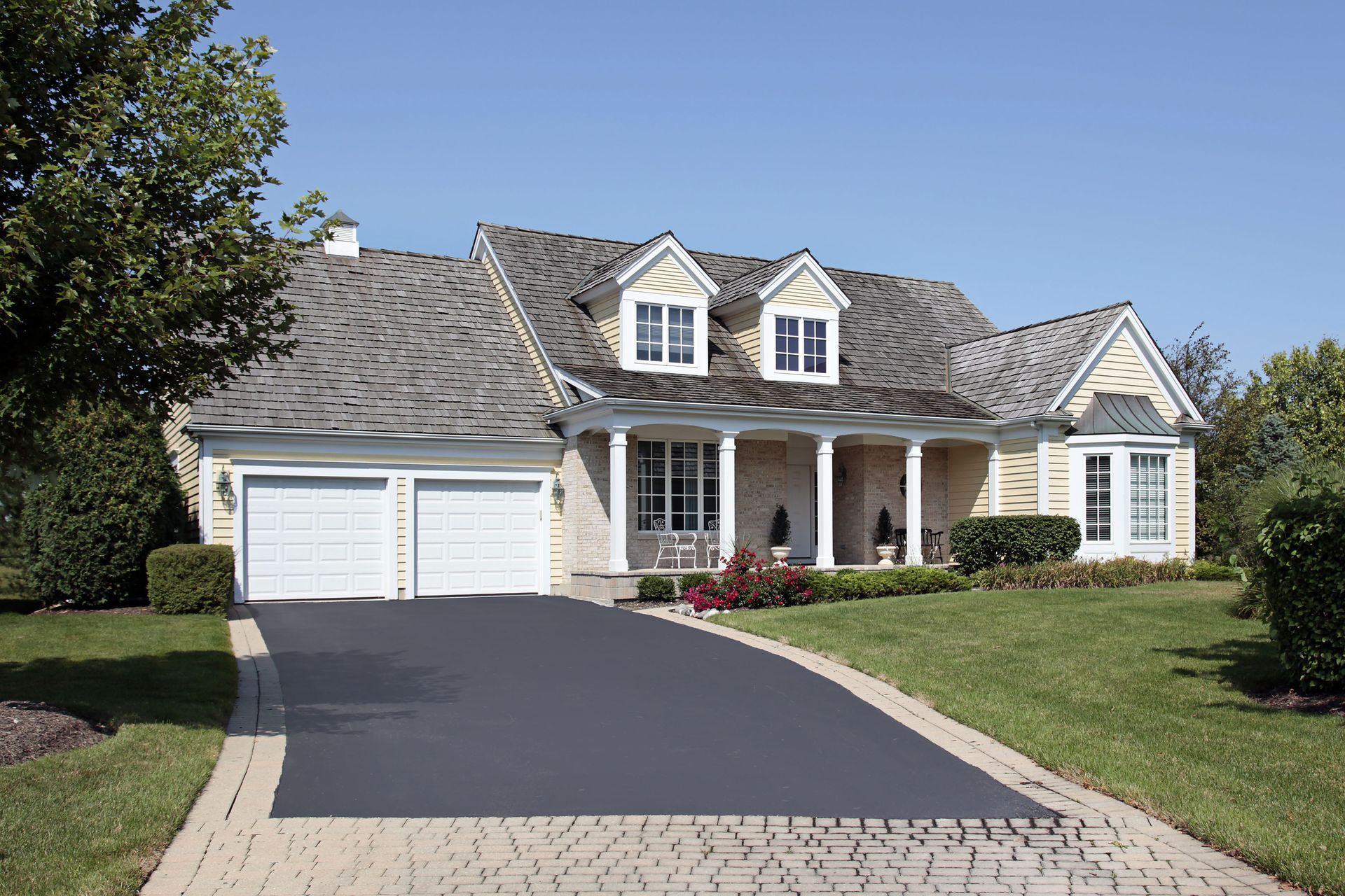 Yellow house with white trim, two-car garage, and long asphalt driveway on a sunny day.