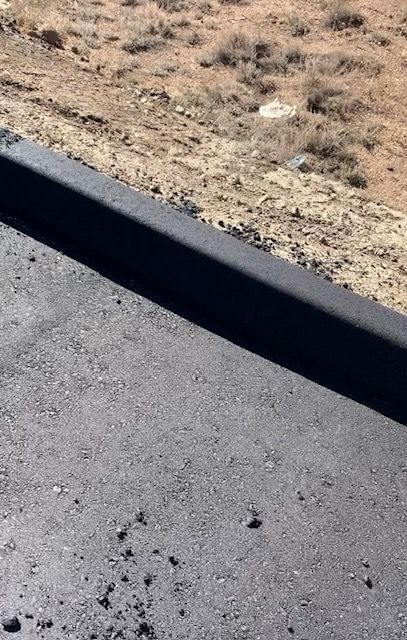 Black asphalt road with dark curb, dry brush hillside in background.