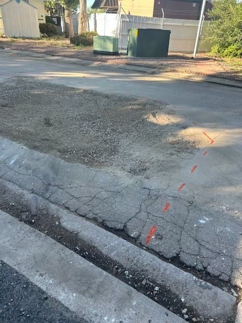 Cracked concrete curb, asphalt road, gravel, construction area marked with orange lines.