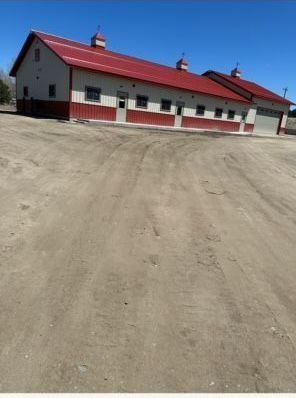 Red-roofed barn-style building with red and white siding under a clear blue sky, parked on a dirt lot.