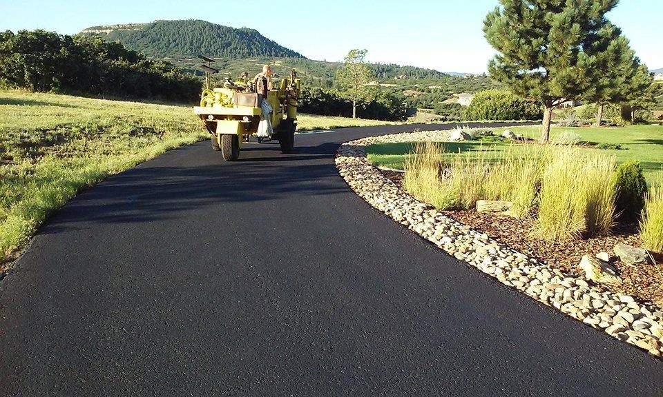 Asphalt driveway with truck, along a landscaped area with grass and rocks, under a sunny sky.