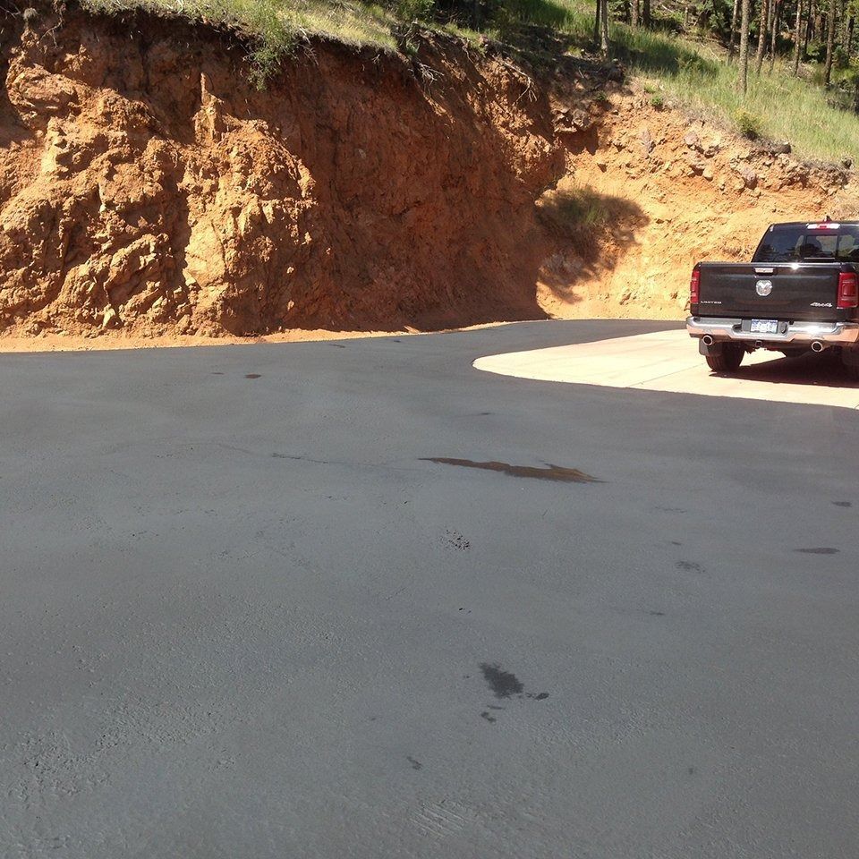 A black pickup truck parked on a curved asphalt road next to a red-brown dirt embankment.
