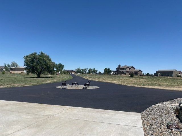 Paved road leading to houses under a blue sky, with three decorative animal statues in a circular island.