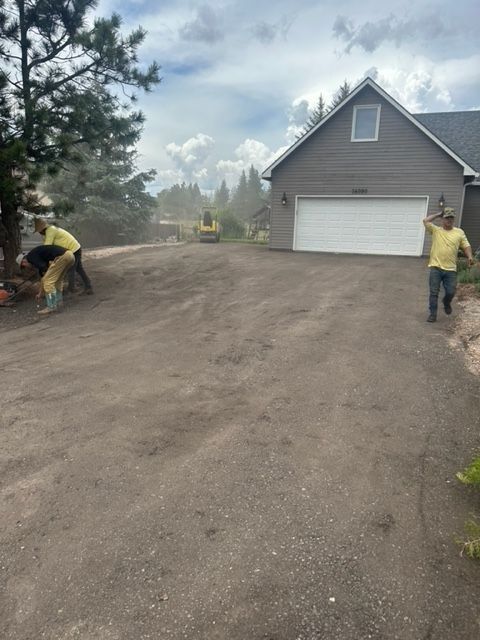 Three workers spread gravel on a driveway. House with attached garage in the background. Cloudy sky.