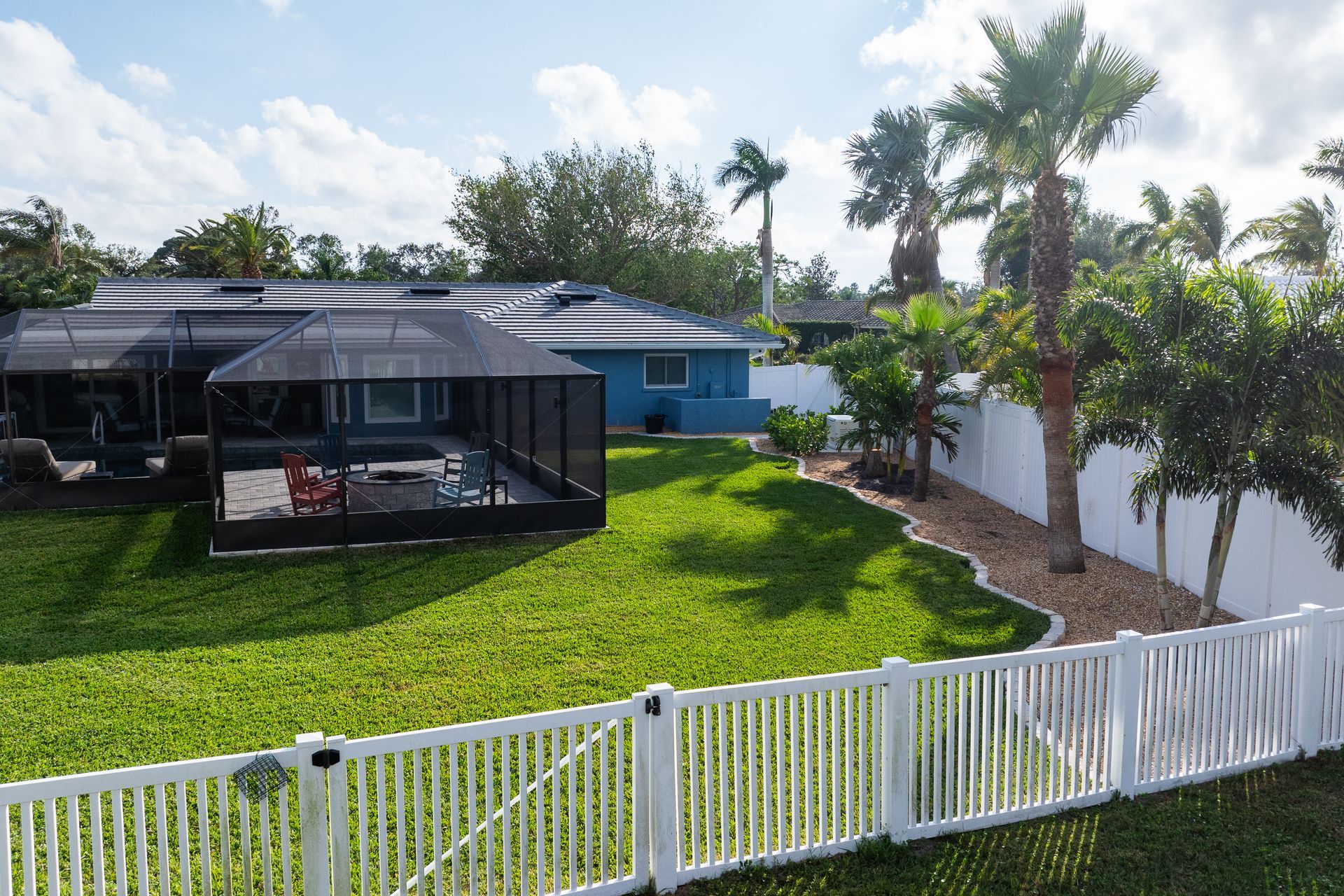 The backyard of a house with a white fence and palm trees