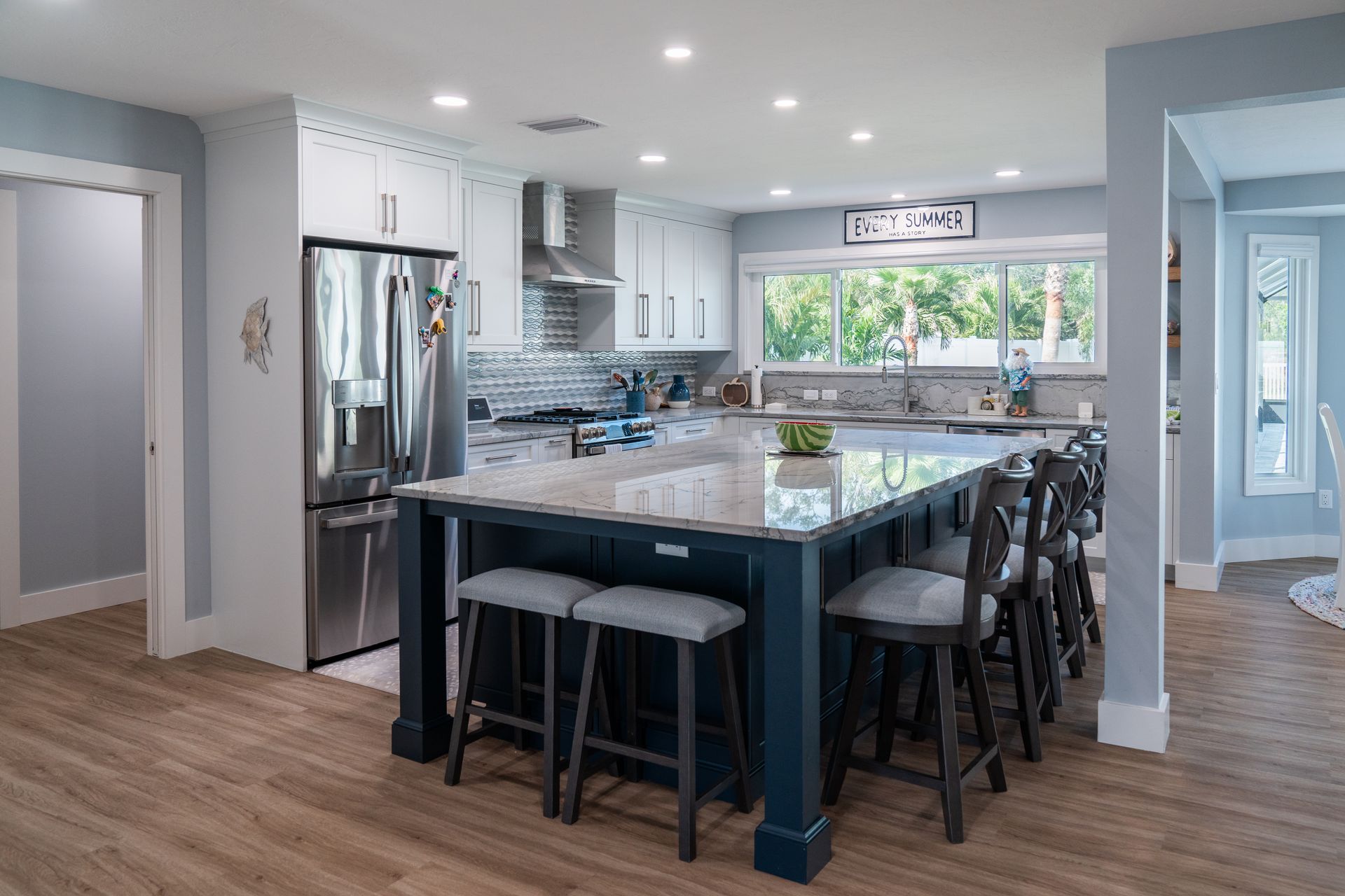 A kitchen with a large island, stools, and a refrigerator.