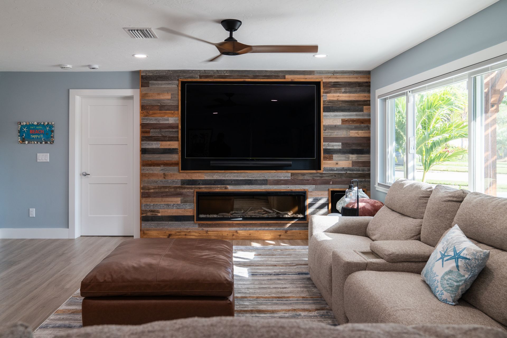 A living room with a couch, ottoman, television, and fireplace.