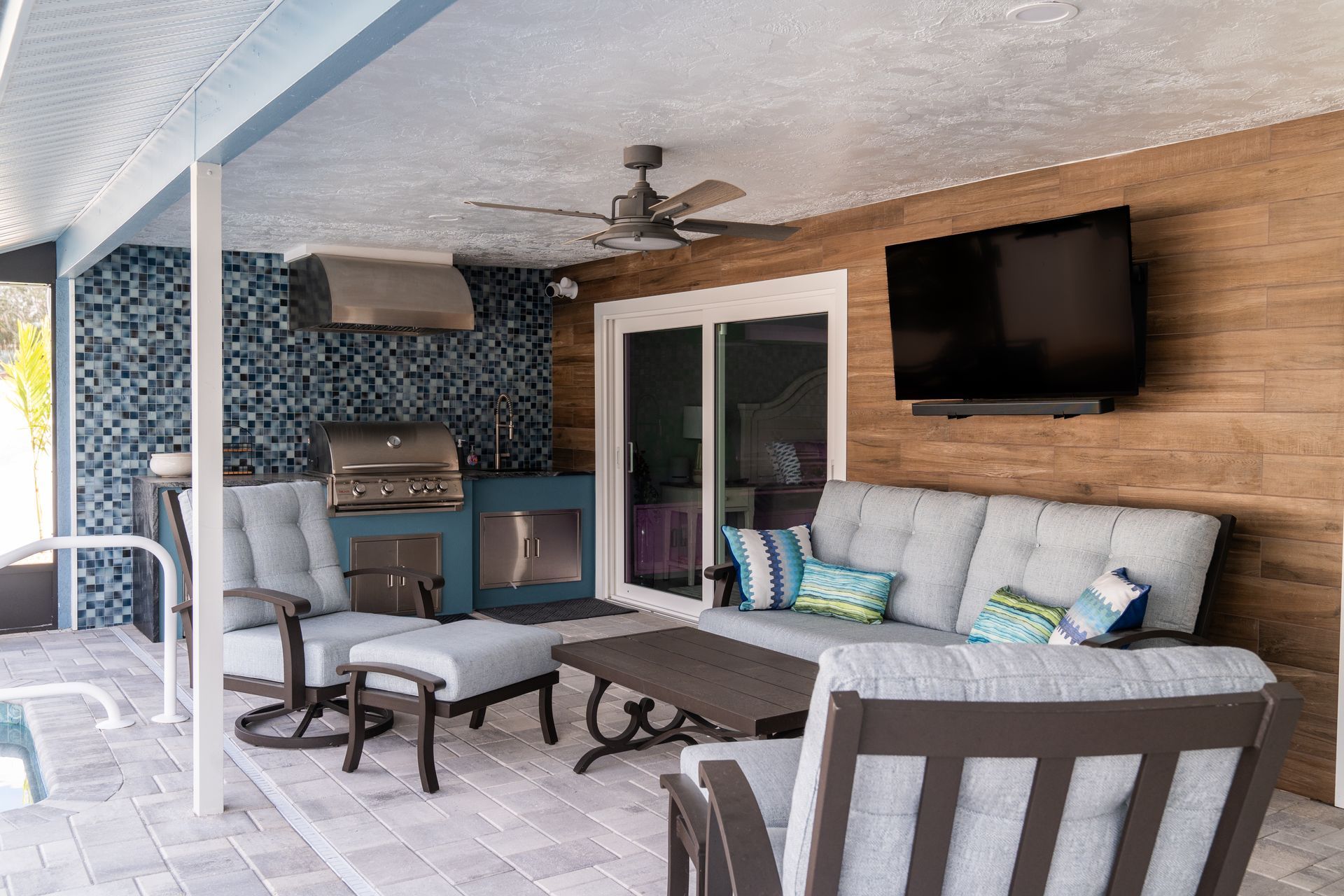 A patio with a couch, chairs, table and television.