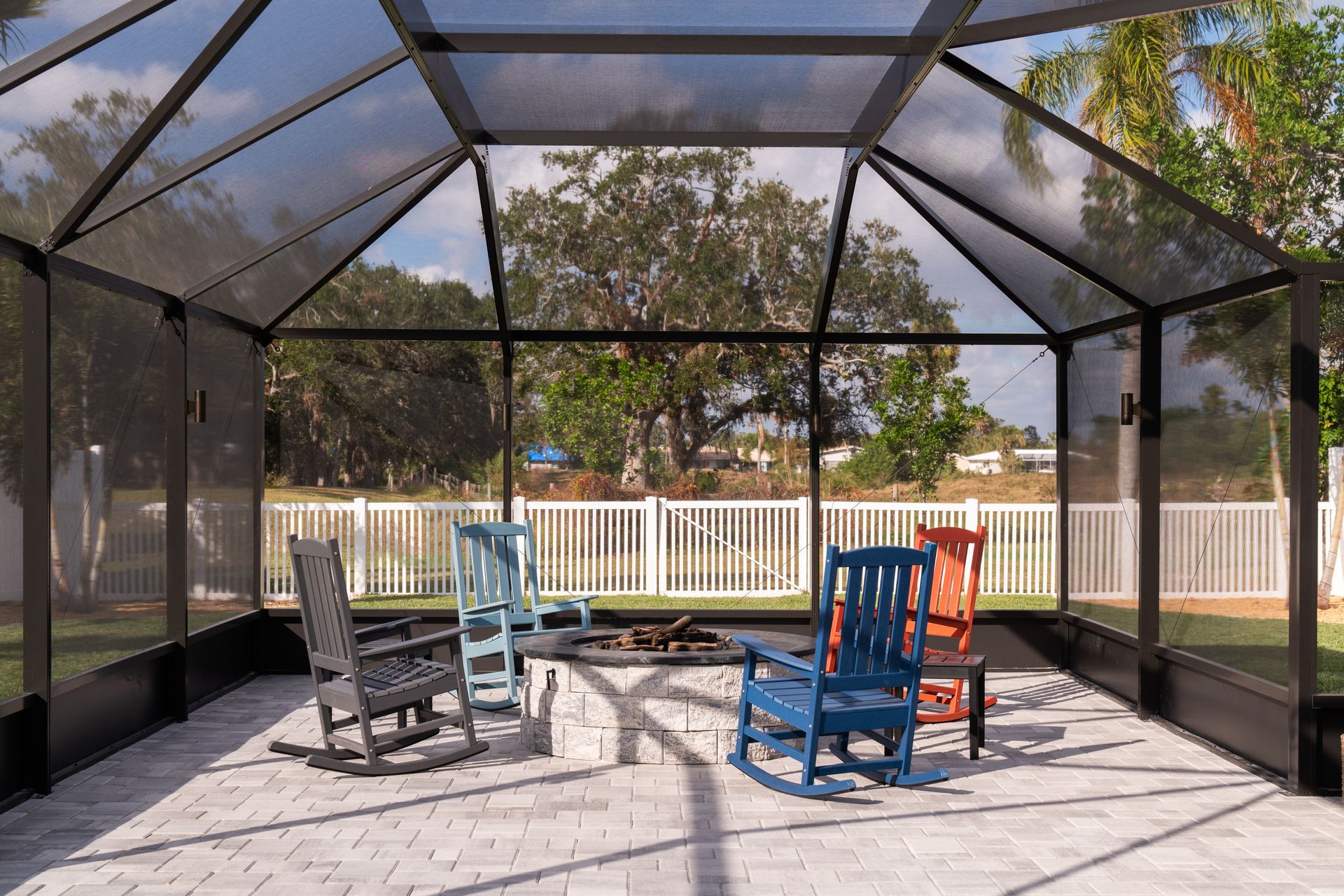 A screened in porch with rocking chairs and a fire pit.
