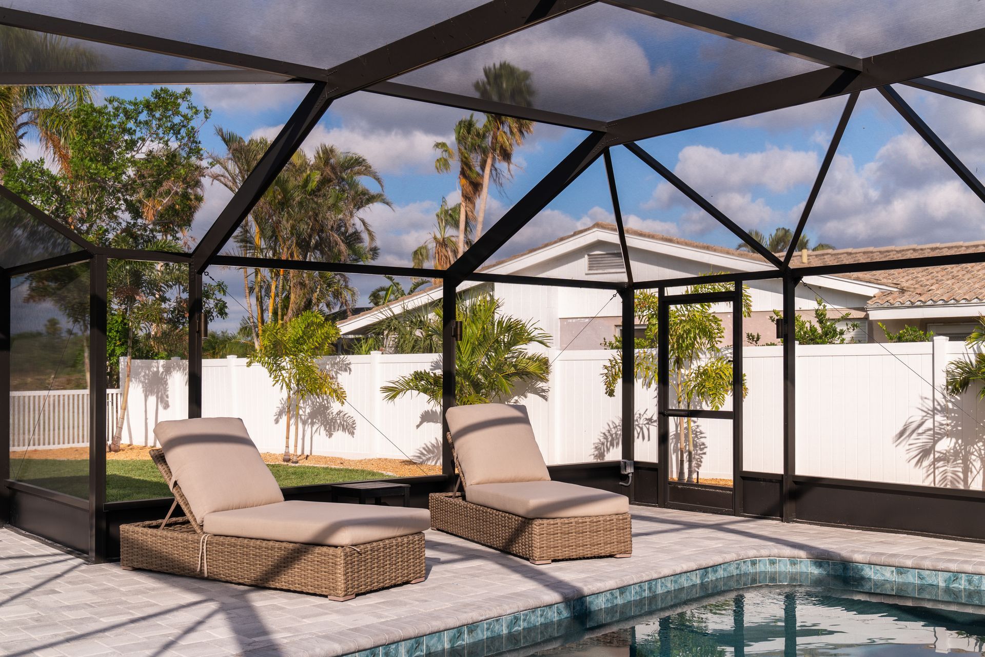 Two lounge chairs are sitting next to a swimming pool in a screened in area.