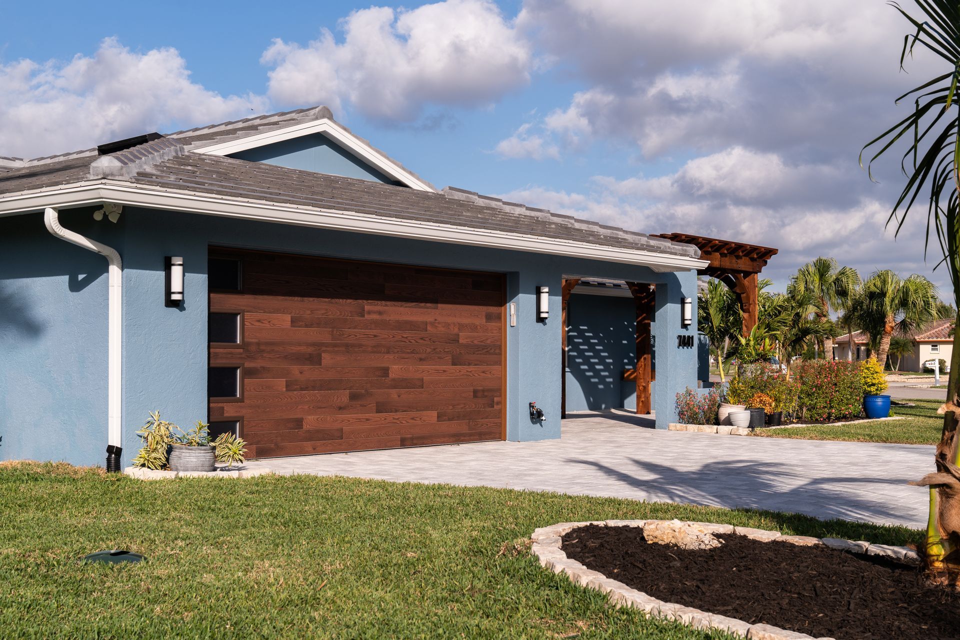 A blue house with a wooden garage door is sitting on top of a lush green lawn.