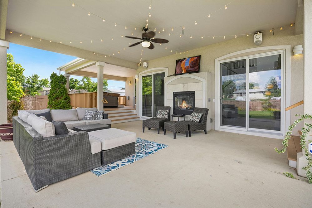 A patio with a couch , chairs , a fireplace and a ceiling fan.