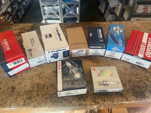 A bunch of boxes of spark plugs are sitting on a wooden table.