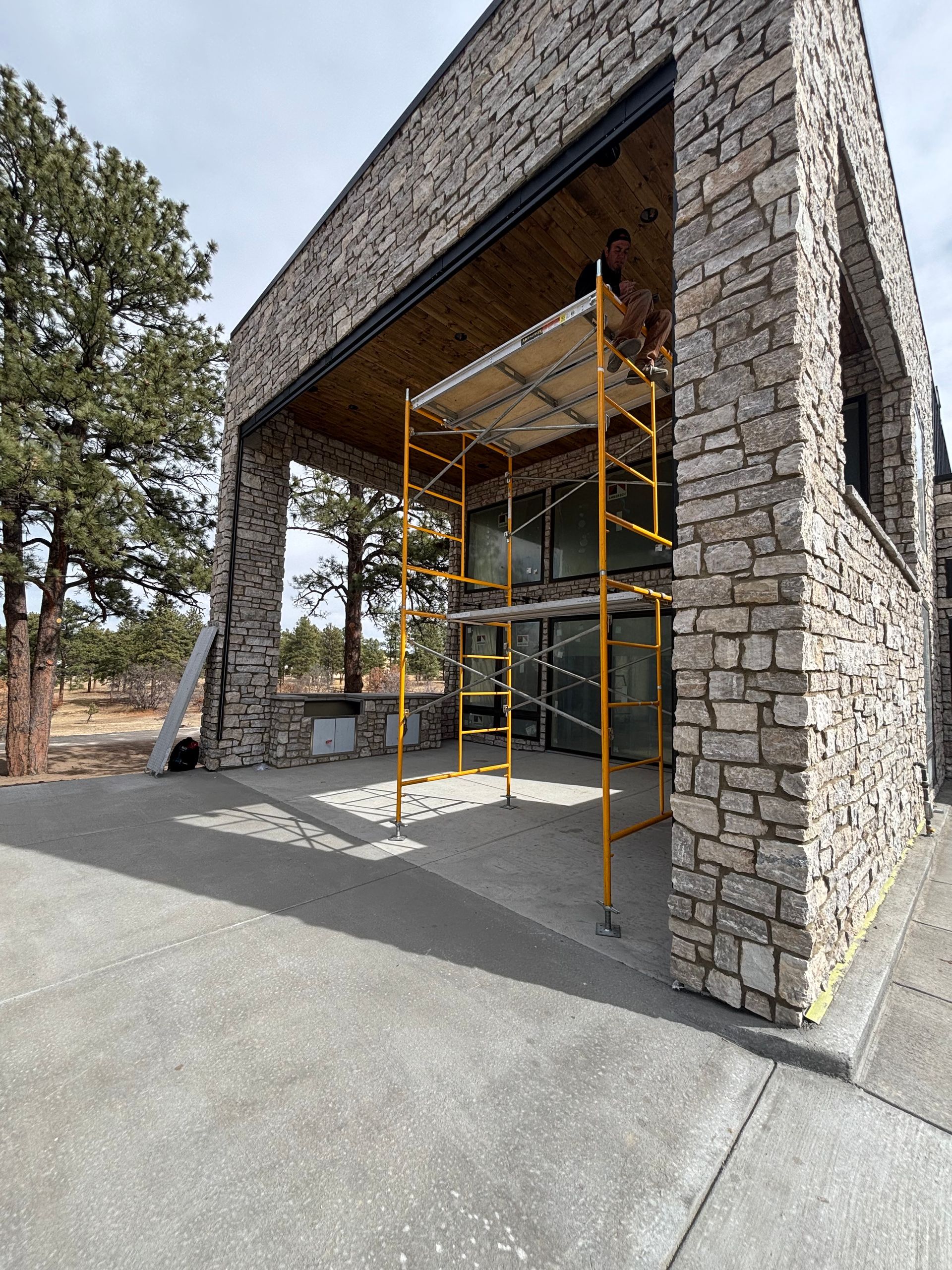 Yellow scaffolding at a stone building entrance with a glass facade and concrete walkway