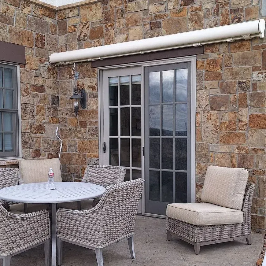 Stone patio with wicker table and chairs beside French doors and a wall-mounted awning