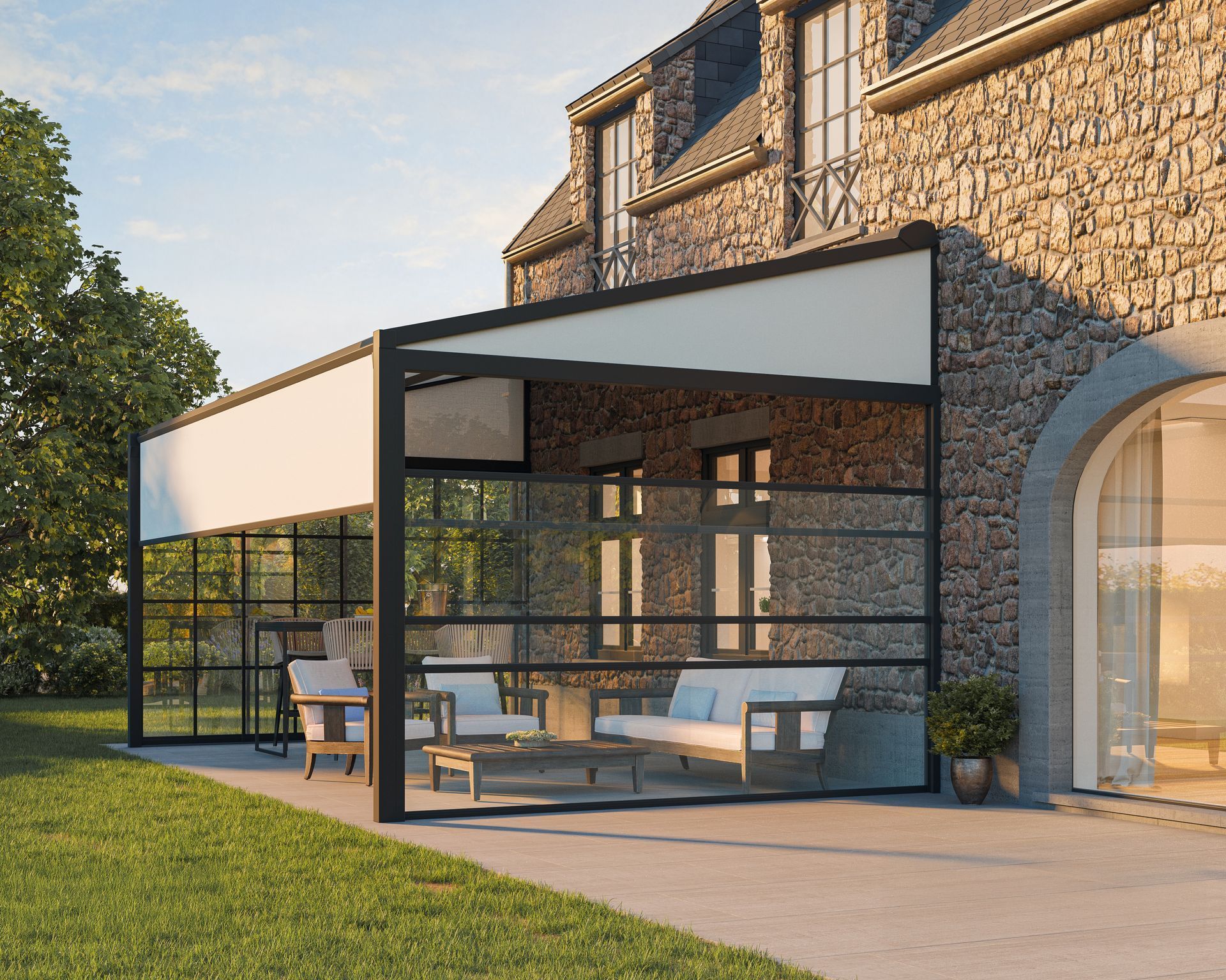 Modern stone house patio with glass canopy, outdoor seating, and green lawn in warm sunlight
