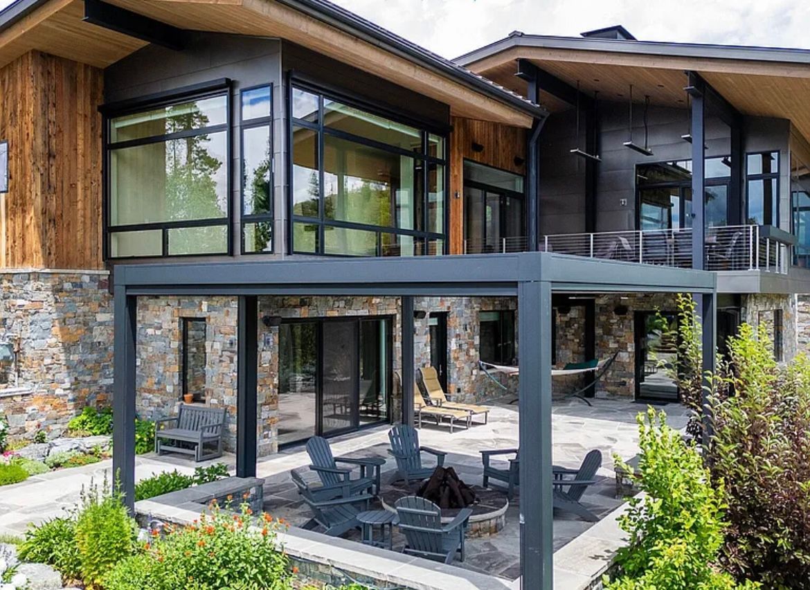 Modern house with large windows, dark metal balcony, and stone patio with outdoor seating