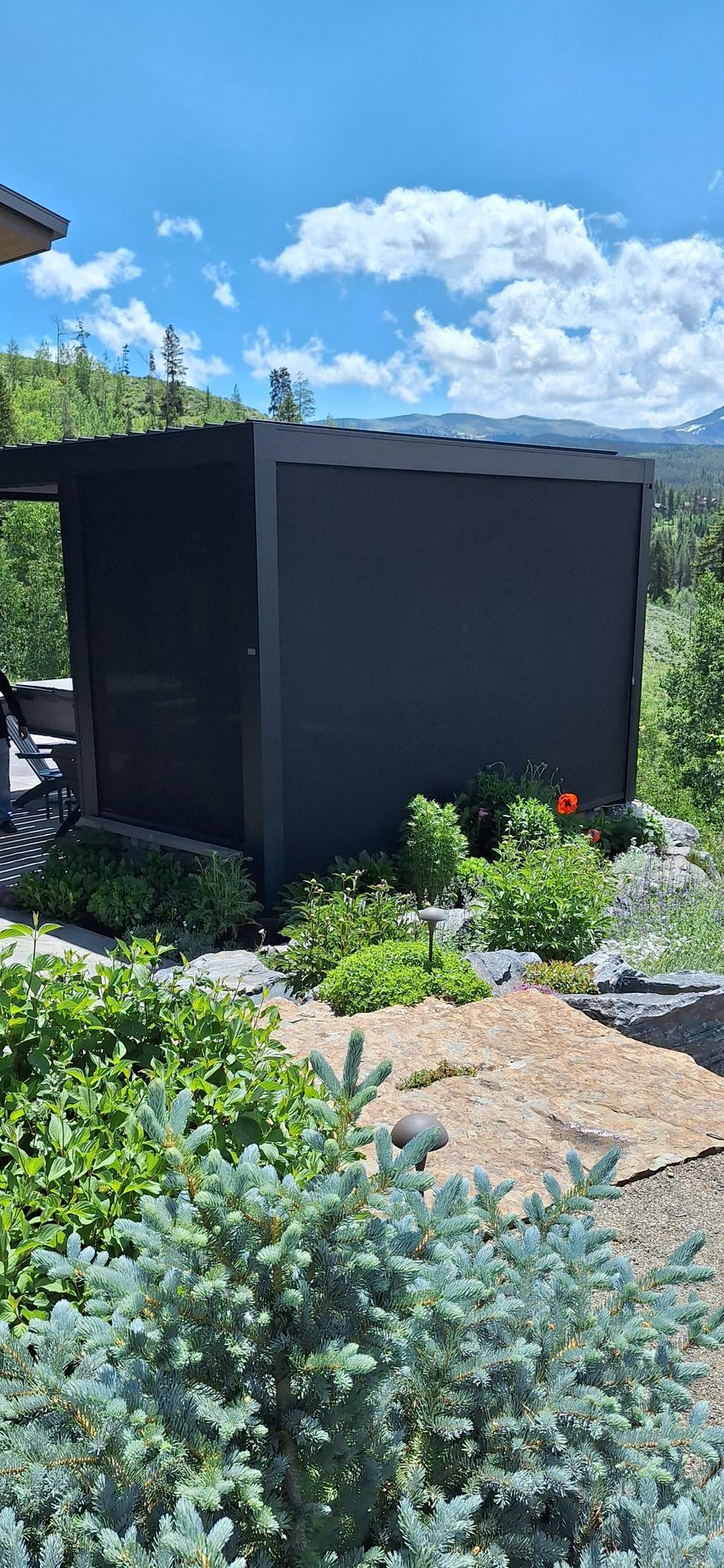 Dark outdoor shed in a sunny garden with shrubs, gravel, and blue sky