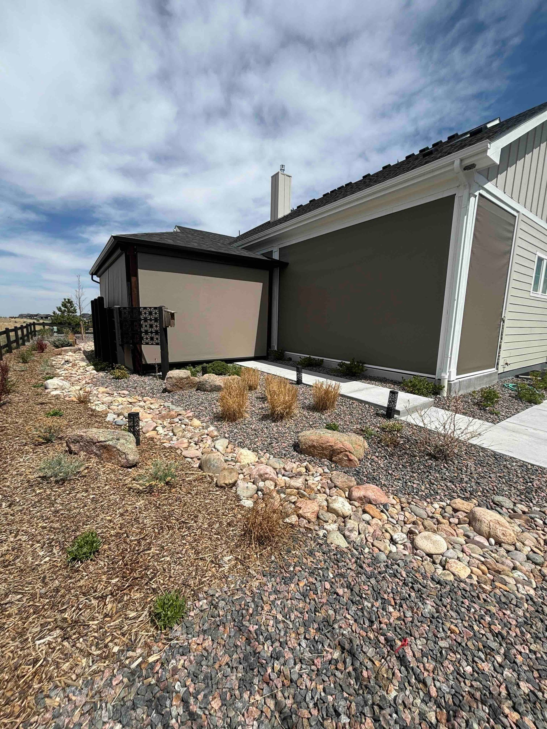 Modern house exterior with gray siding, gravel landscaping, and a small covered porch under a blue sky