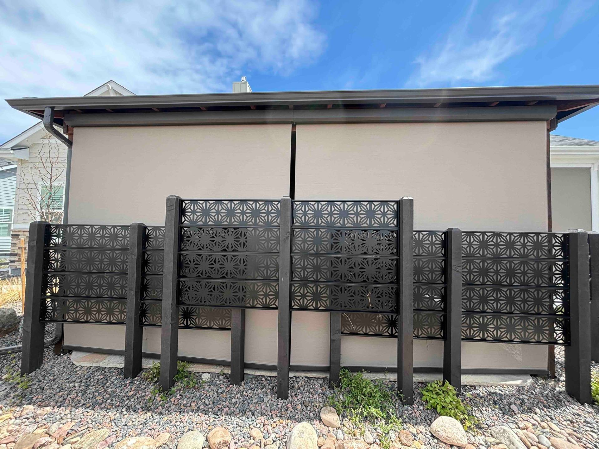 Black decorative privacy fence panels in front of a beige building under a blue sky.