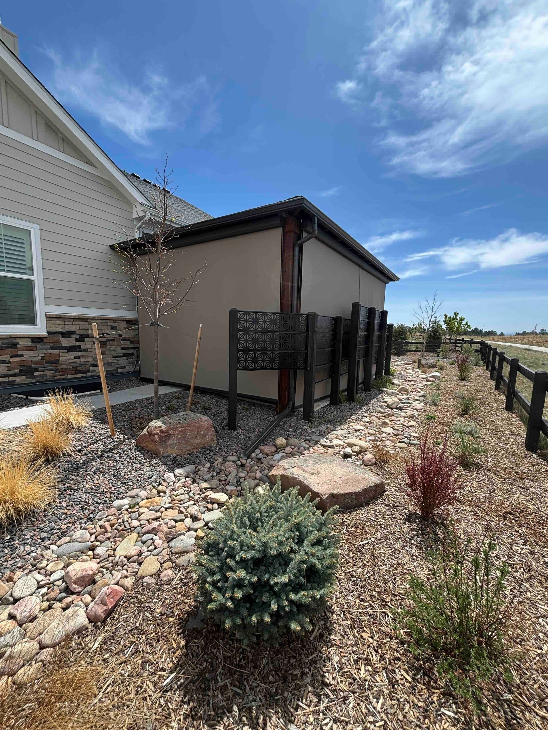 Side yard with a small shed, black fence, gravel landscaping, and a house under a blue sky