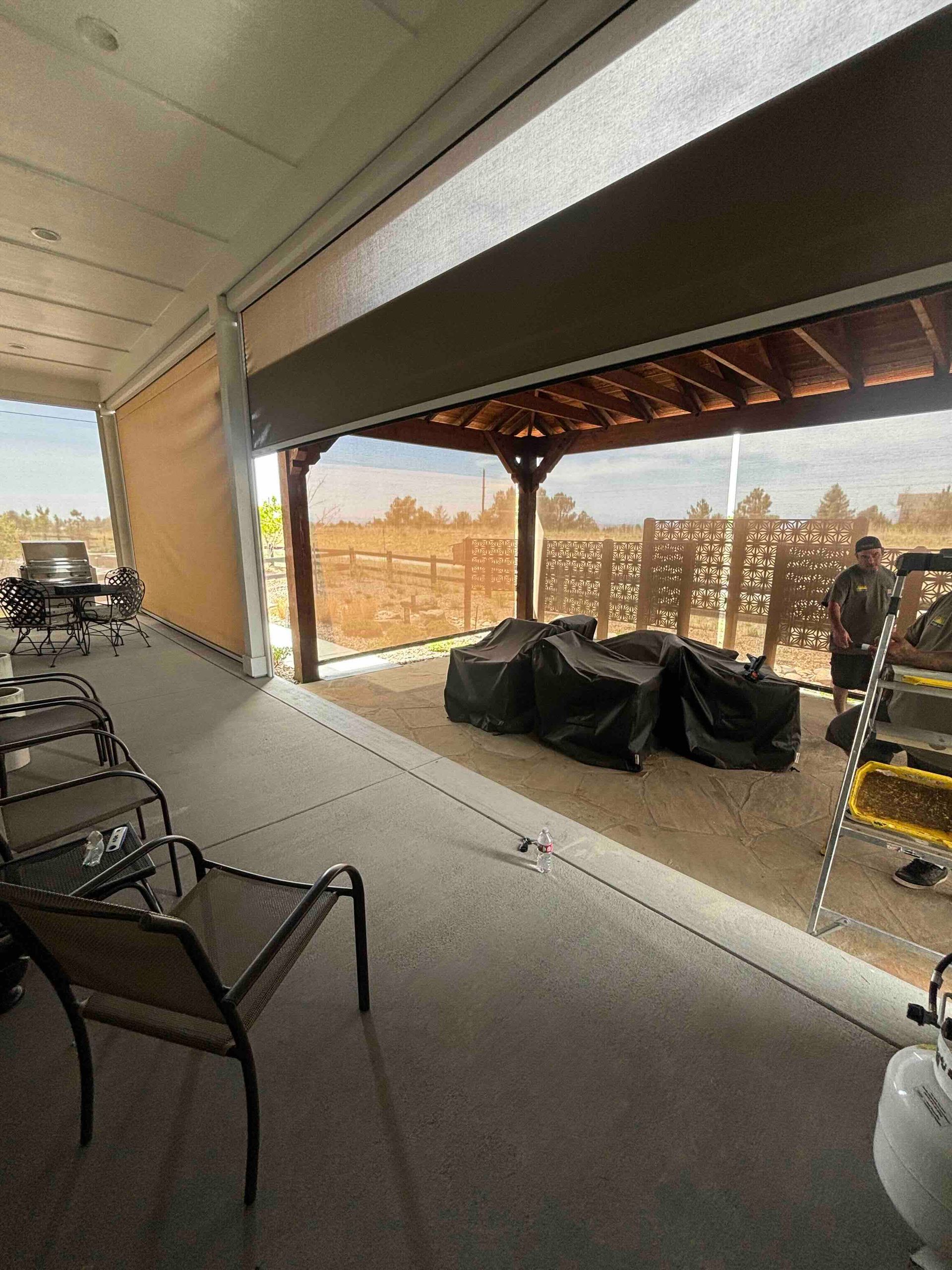 Covered patio with chairs, grill under a gazebo, and a person standing near the railing.