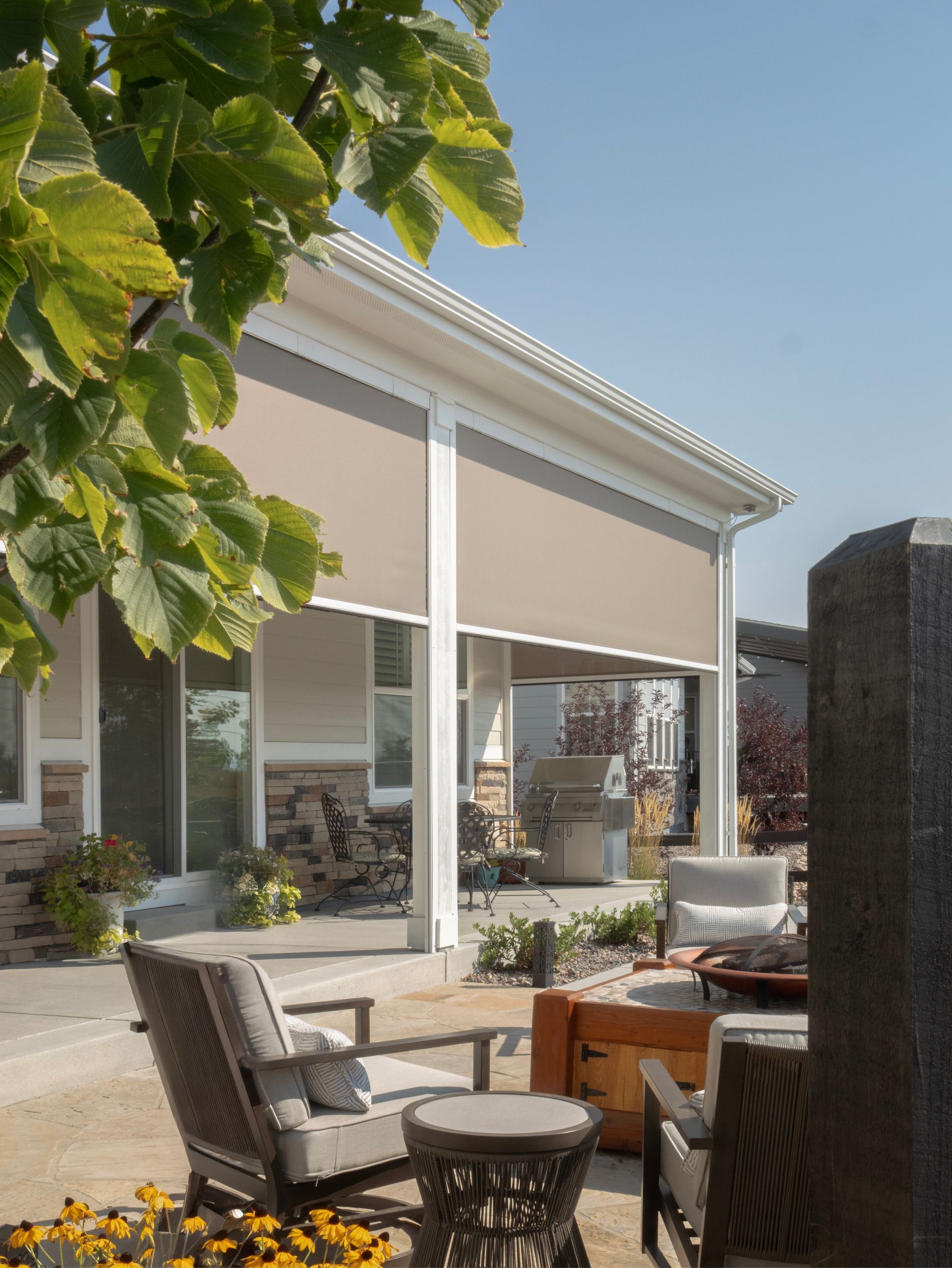 Patio with outdoor chairs and table beside a house, under a white awning with leafy branches overhead