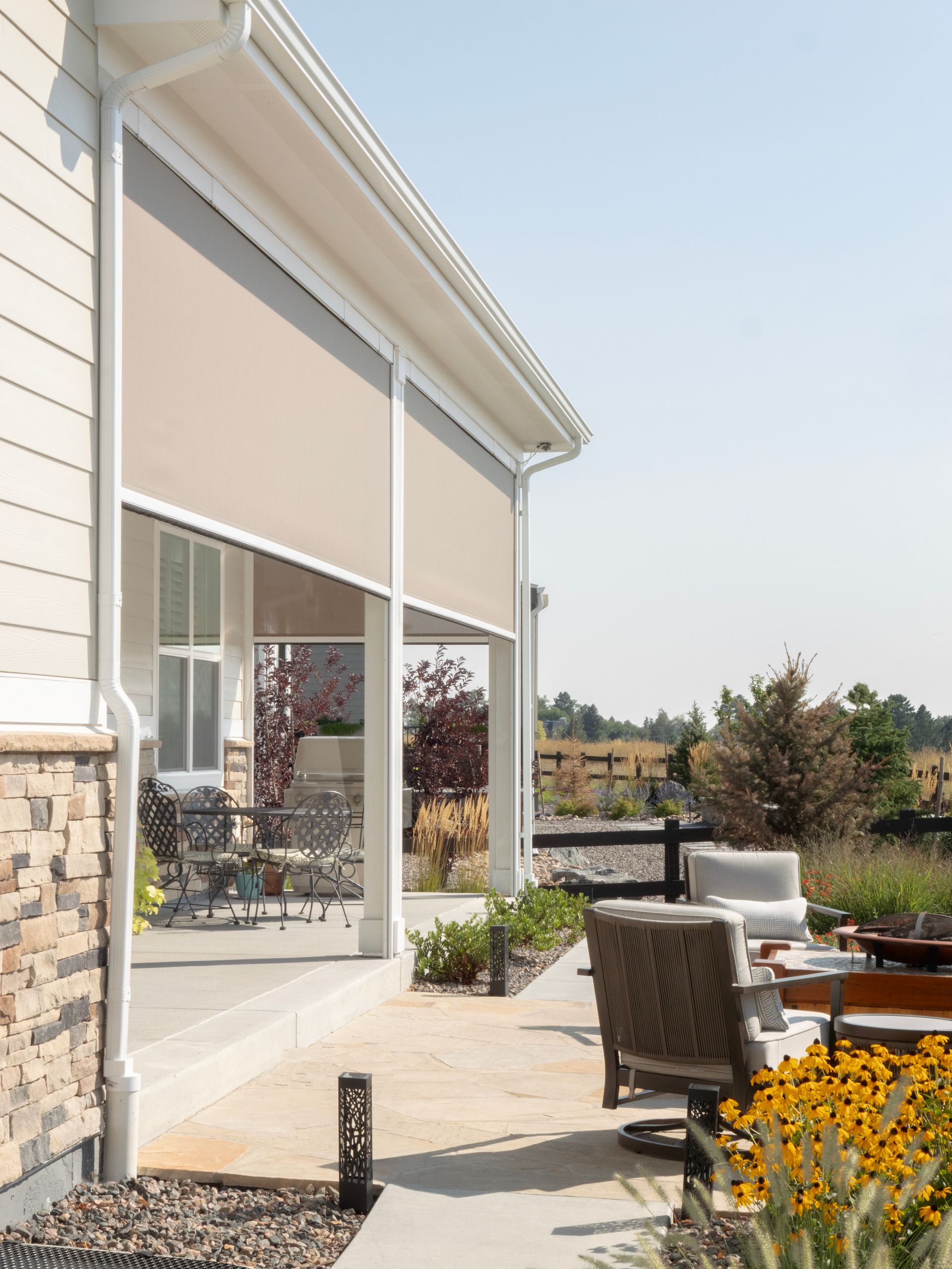 Patio outside a modern house with outdoor chairs, flowers, and a view of the landscape