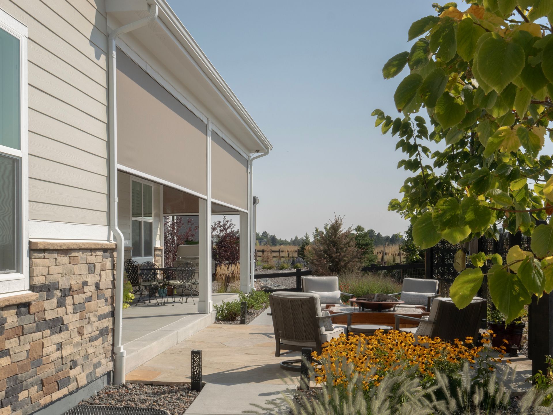 Patio beside a house with stone siding, outdoor chairs, and flowers in bright daylight