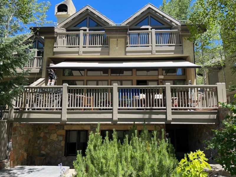 Two-story house with beige balconies, stone accents, and green trees in front