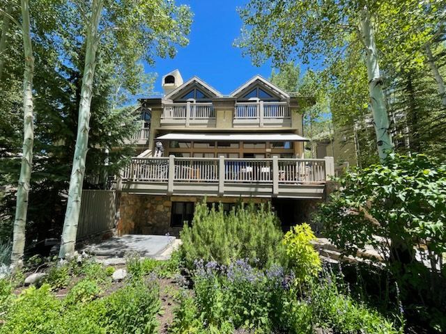 Wooden cabin with multiple decks nestled among tall trees in a sunny forest clearing