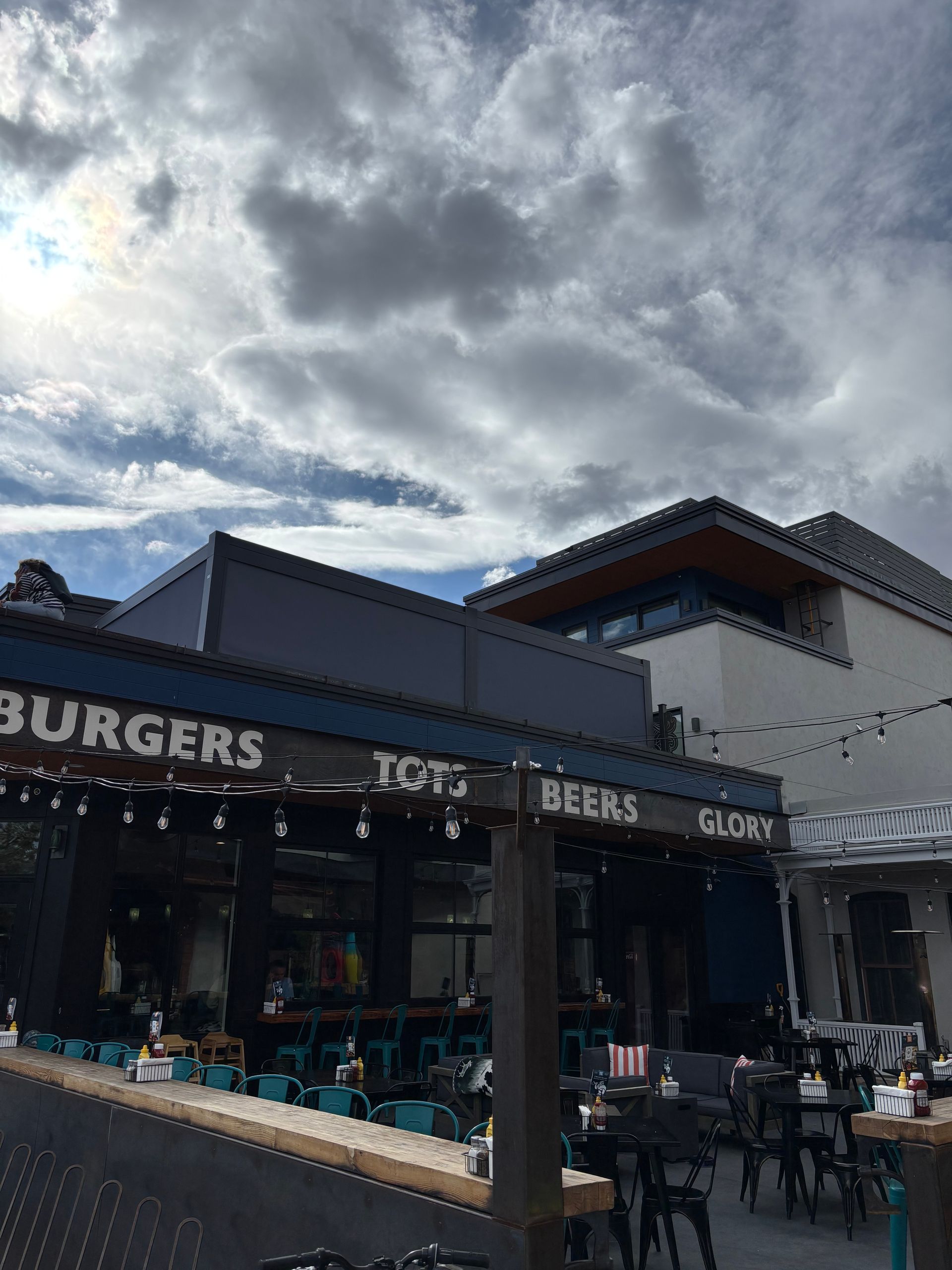 Outdoor burger restaurant with blue awnings and diners under a cloudy sky