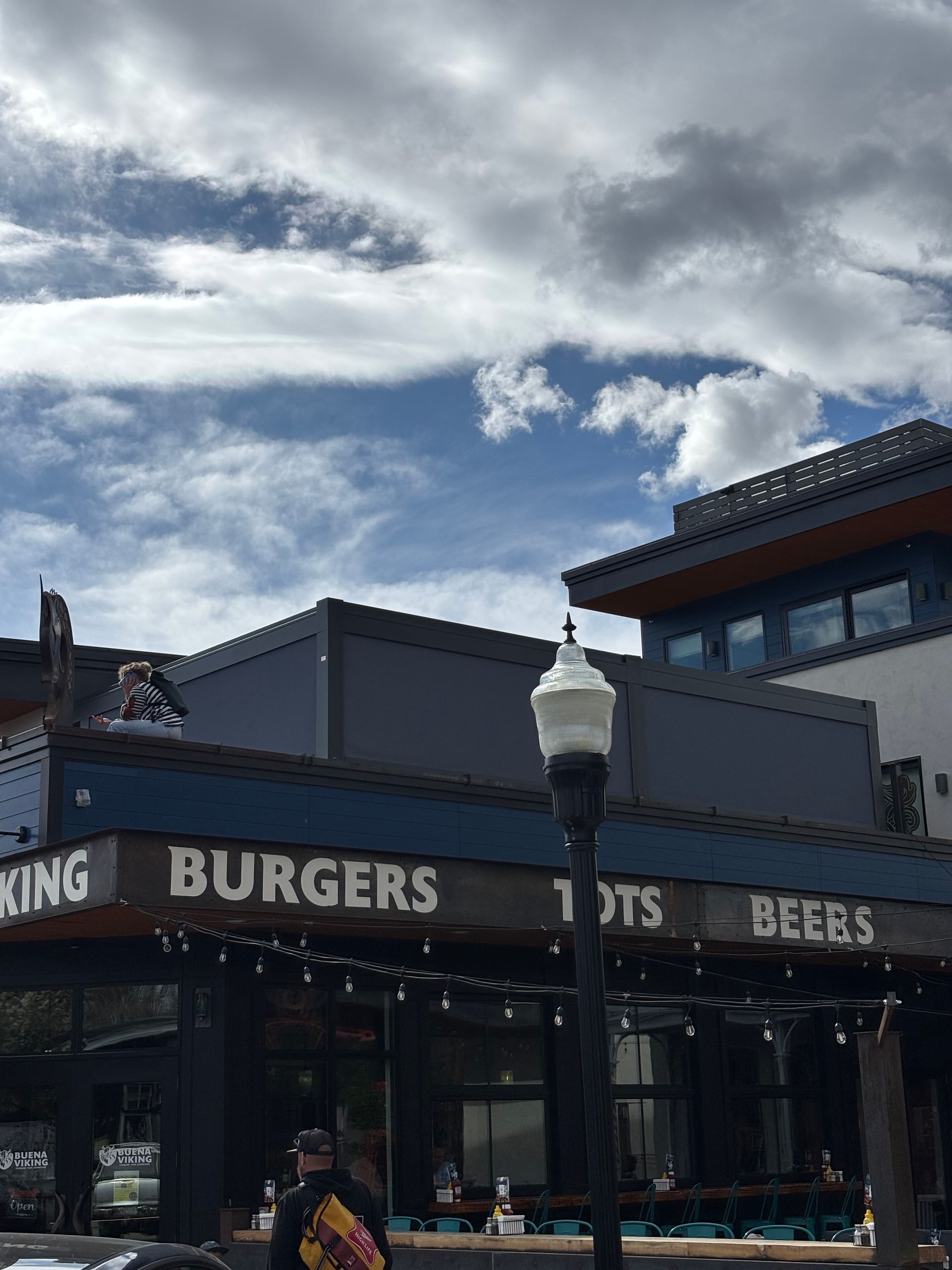 Street-side burger bar with a lamppost, dark awning, and cloudy sky above.