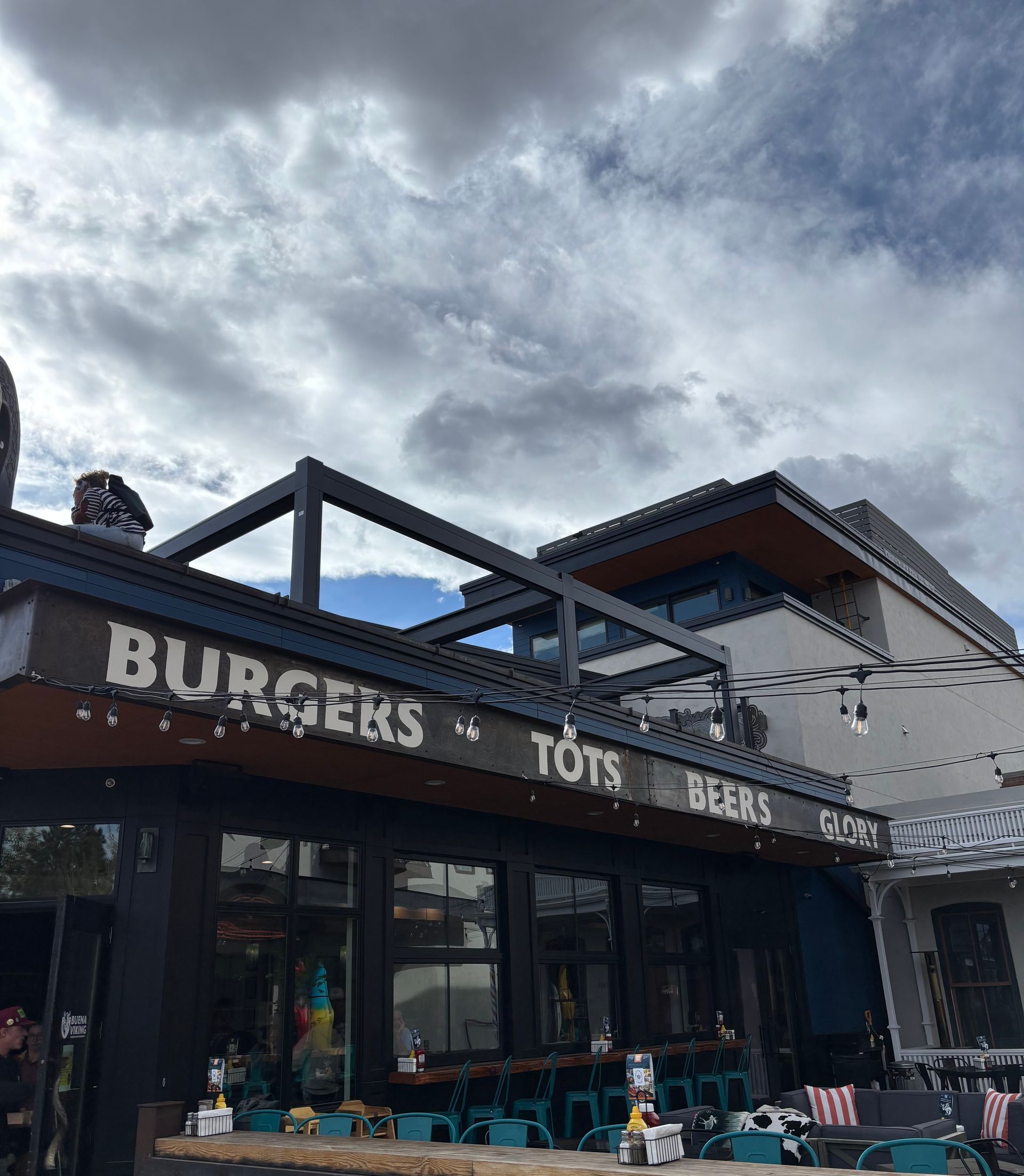 Burger and drinks storefront with outdoor seating under a cloudy sky