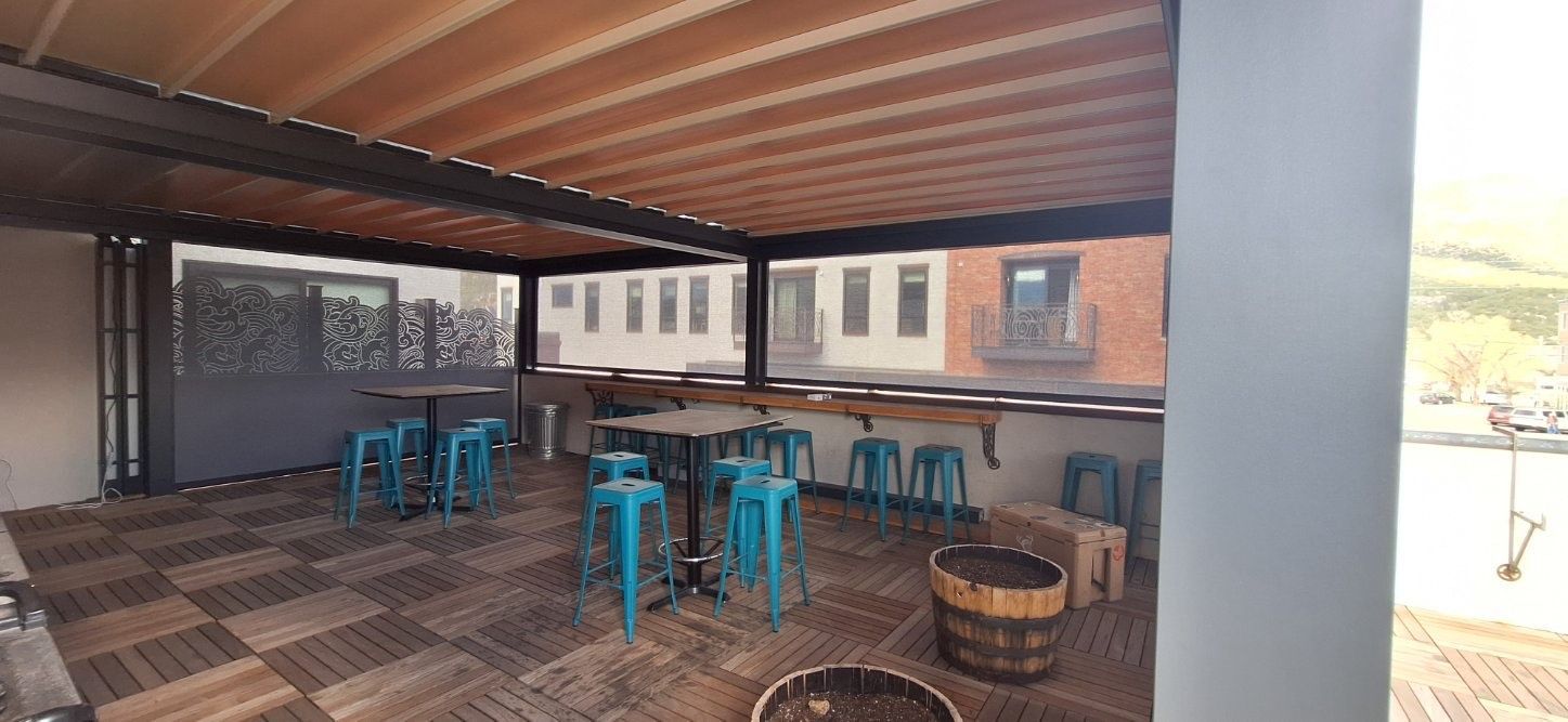 Covered outdoor seating area with turquoise tables and chairs, wooden ceiling, and woven bar stools